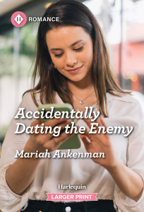 Cover for Accidentally Dating The Enemy by Mariah Ankenman Woman with brown hair staring at a phone in her hands smiling